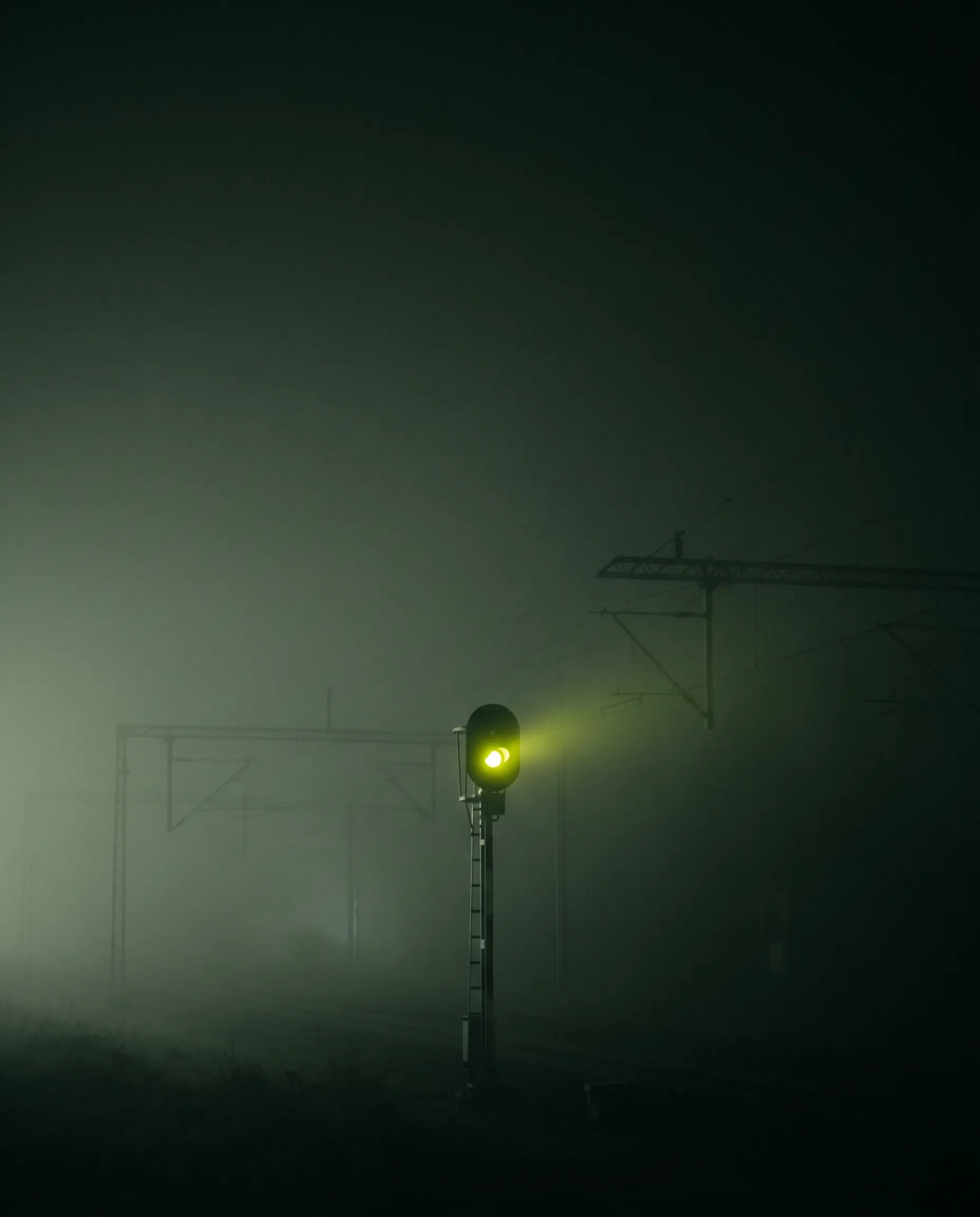 A lone railway signal glowing green in dense night fog.