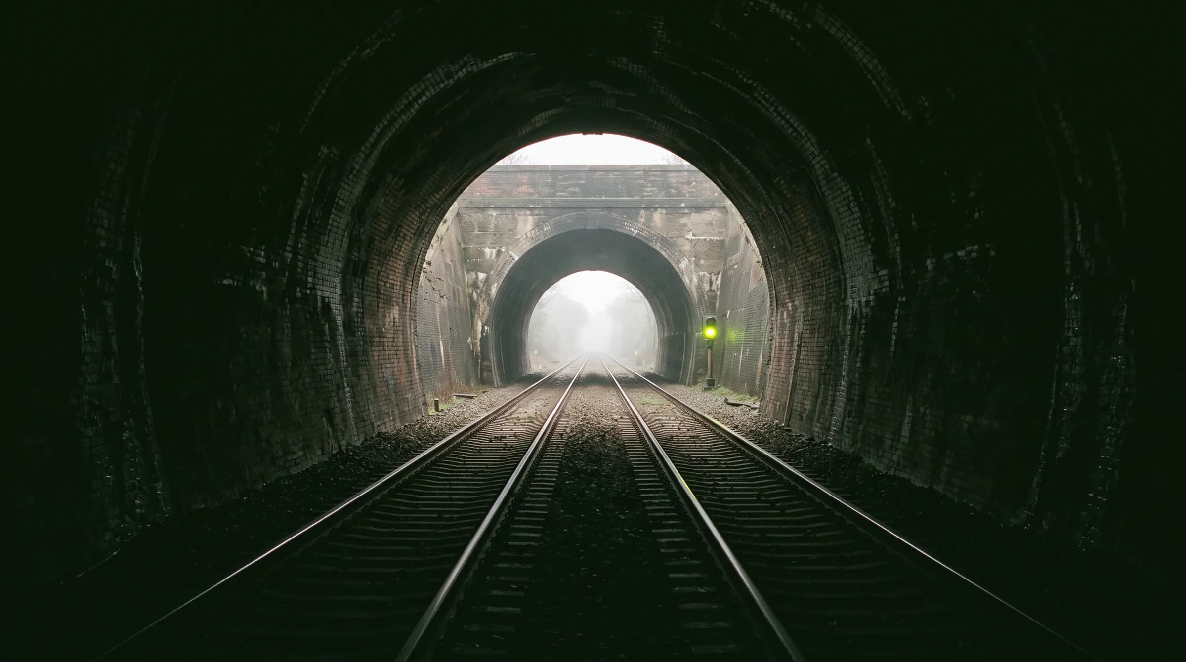 View from inside a railway tunnel toward the bright exit, rails running straight out.